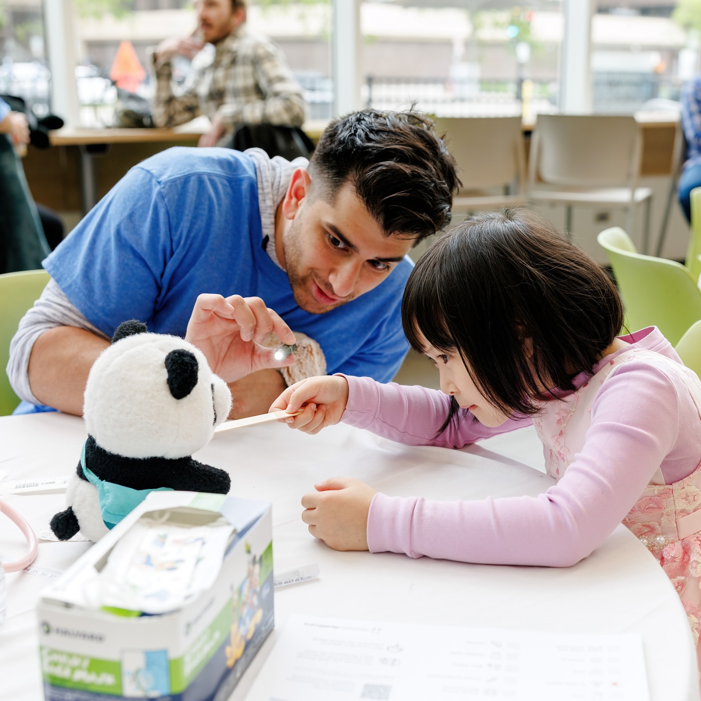 Little girl and a male nurse together provide a pretend medical examination on her panda teddy bear at an event hosted by a Minneapolis hospital to help children get comfortable around medical tools and processes.